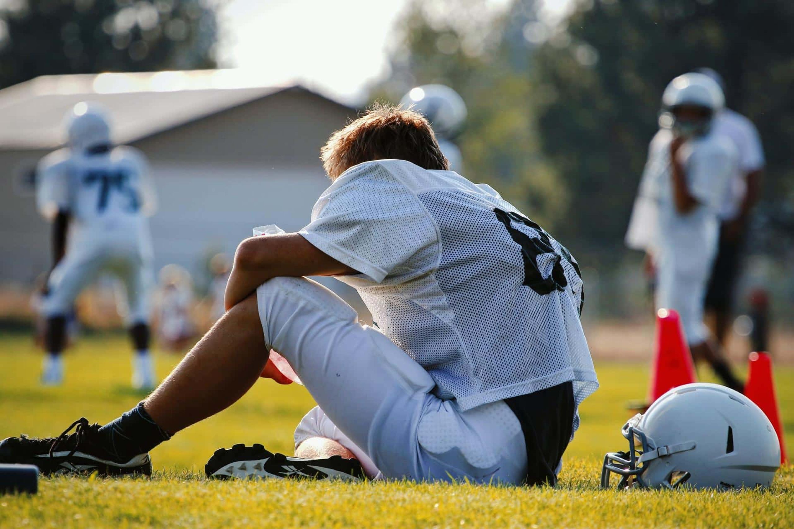 football player outside sitting on the field while others practice
